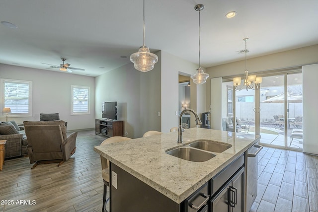 kitchen featuring sink, hanging light fixtures, light hardwood / wood-style flooring, an island with sink, and light stone countertops