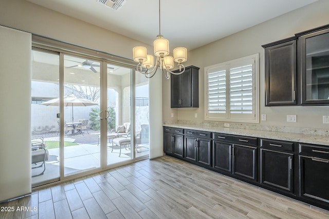 kitchen featuring hanging light fixtures, ceiling fan with notable chandelier, light hardwood / wood-style flooring, and light stone countertops