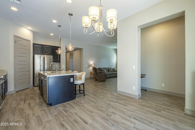 kitchen with a kitchen island with sink, pendant lighting, light stone counters, and light wood-type flooring