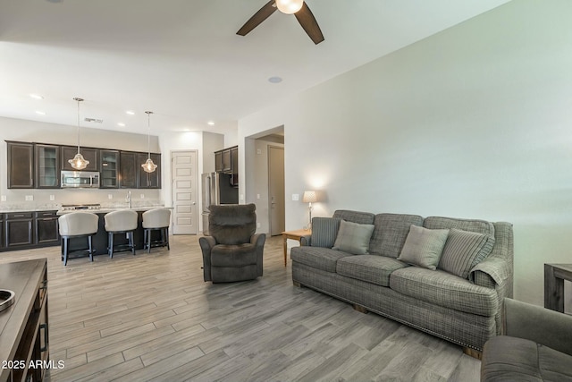 living room with ceiling fan, sink, and light wood-type flooring