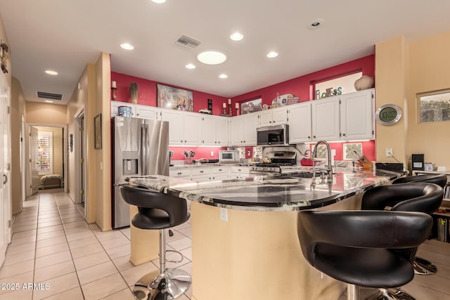 kitchen featuring light tile patterned floors, appliances with stainless steel finishes, white cabinetry, a kitchen bar, and kitchen peninsula