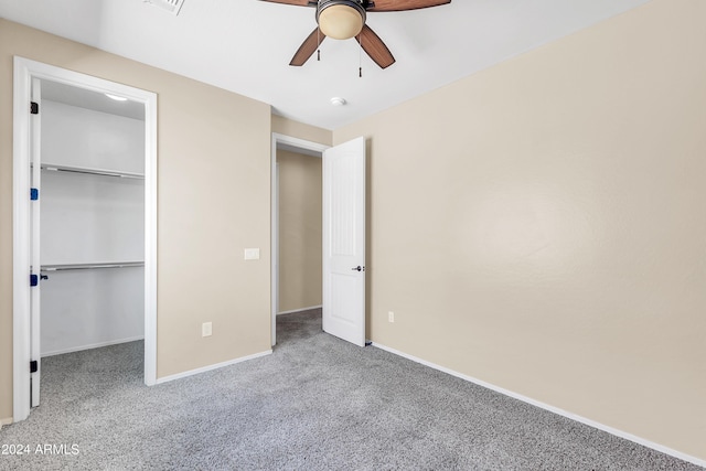 unfurnished bedroom with carpet, a walk in closet, a closet, ceiling fan, and baseboards