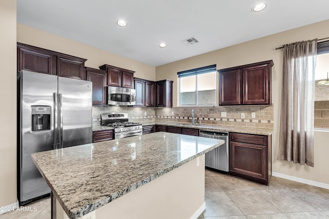 kitchen with stainless steel appliances, a sink, a kitchen island, decorative backsplash, and light stone countertops