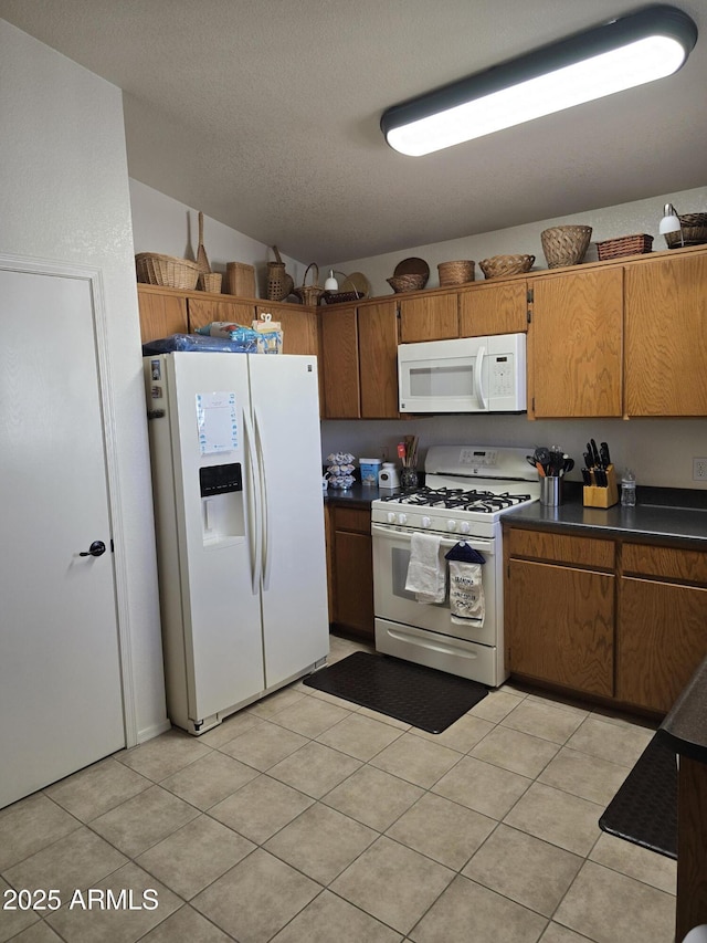 kitchen featuring white appliances, light tile patterned floors, brown cabinetry, dark countertops, and a textured ceiling