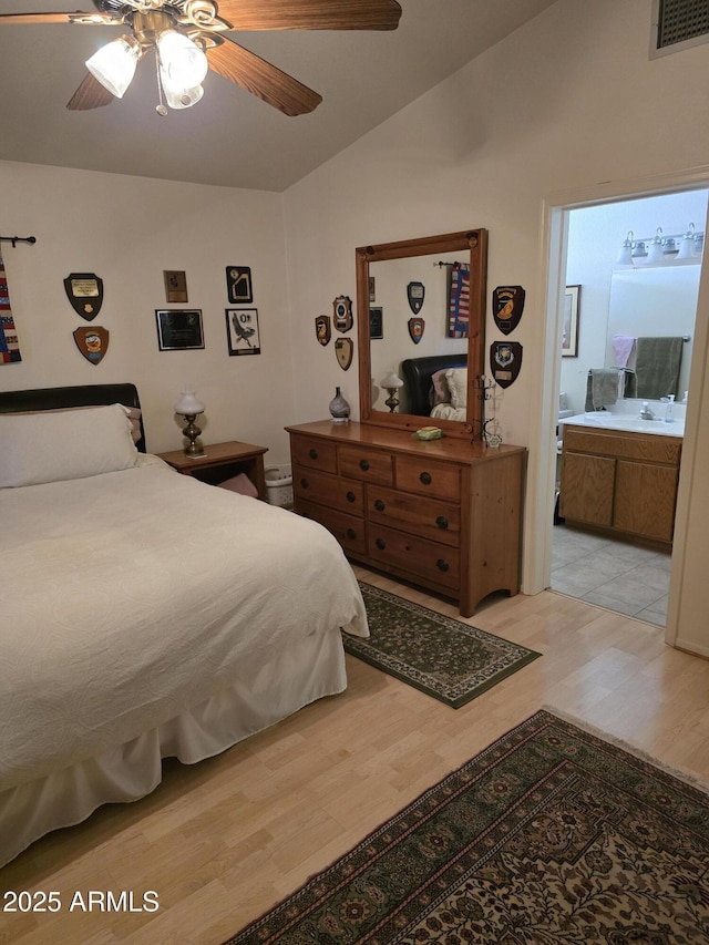 bedroom with lofted ceiling, visible vents, light wood-style flooring, ensuite bathroom, and a sink