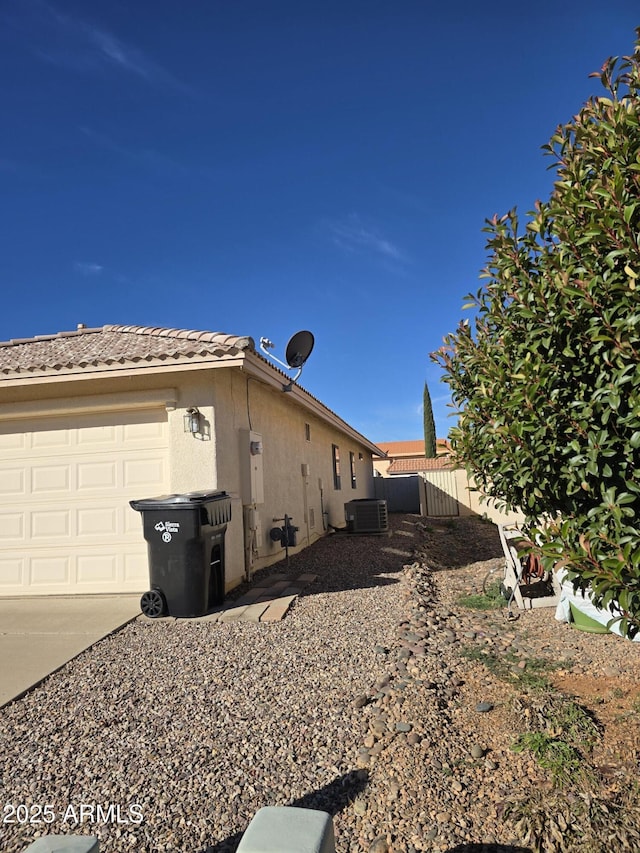 view of home's exterior with central air condition unit, stucco siding, fence, a garage, and a tiled roof