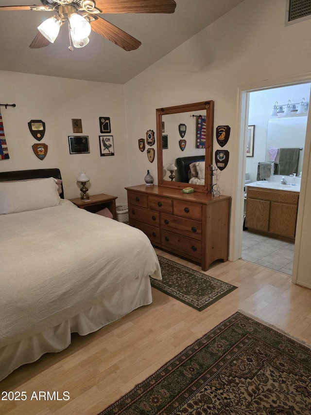 bedroom featuring light wood-style flooring, a sink, vaulted ceiling, visible vents, and connected bathroom