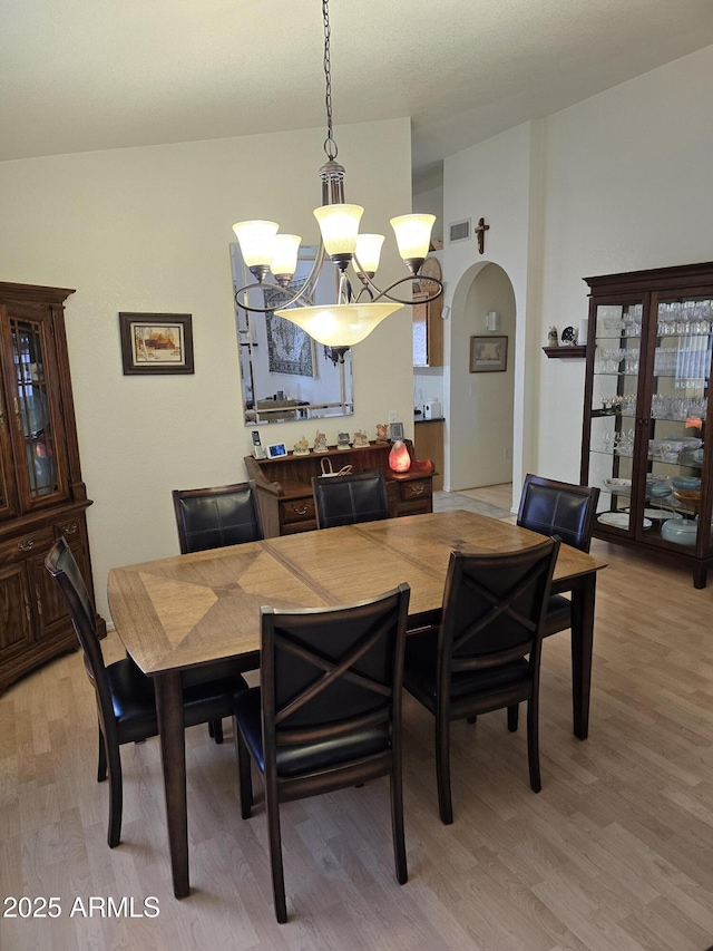 dining area featuring arched walkways, visible vents, an inviting chandelier, and wood finished floors