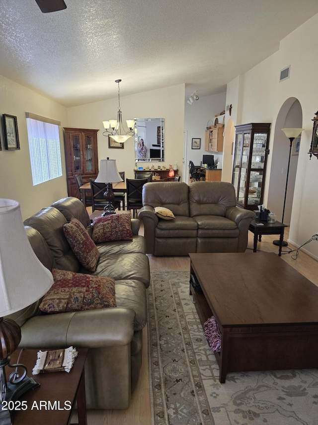 living room with lofted ceiling, a textured ceiling, arched walkways, and a notable chandelier