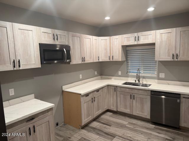 kitchen with light stone countertops, sink, light wood-type flooring, and black dishwasher