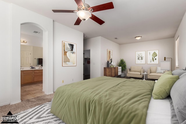 bedroom featuring ensuite bathroom, light colored carpet, and ceiling fan