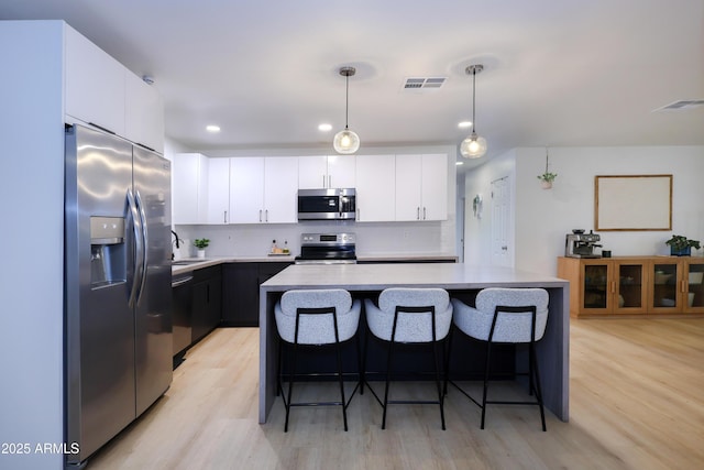 kitchen with light hardwood / wood-style flooring, appliances with stainless steel finishes, hanging light fixtures, tasteful backsplash, and a kitchen island