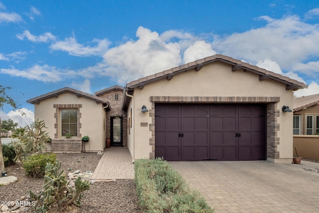 ranch-style home featuring an attached garage, decorative driveway, and stucco siding