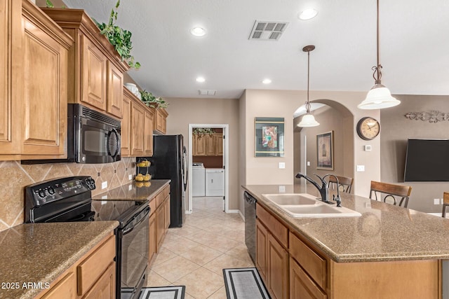 kitchen featuring visible vents, arched walkways, washer and dryer, black appliances, and a sink