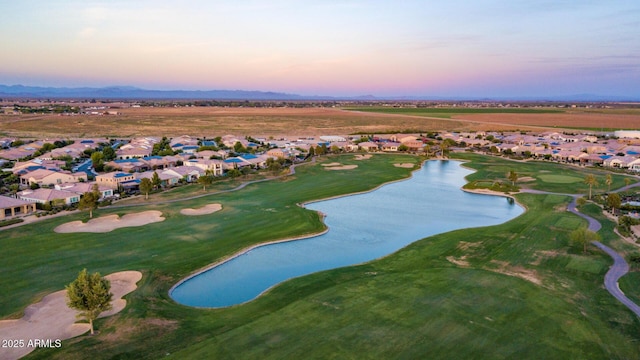 aerial view at dusk featuring a residential view, a water view, and golf course view