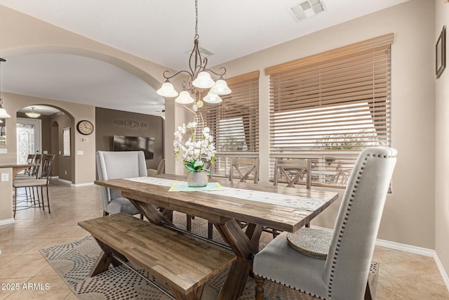 dining space featuring arched walkways, light tile patterned floors, visible vents, a chandelier, and baseboards