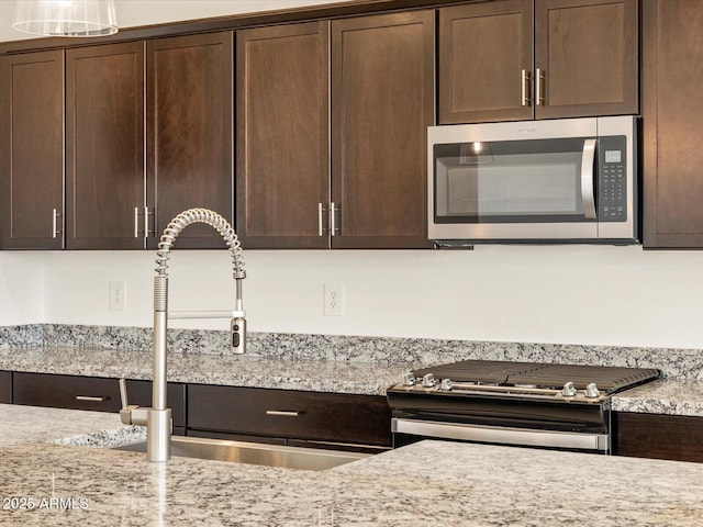 kitchen featuring sink, stainless steel appliances, dark brown cabinets, and light stone countertops