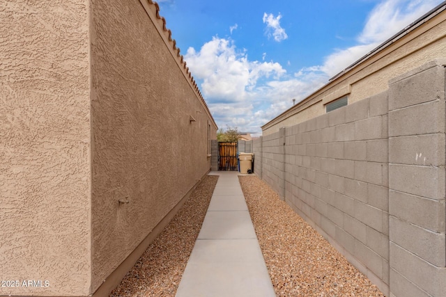 view of side of property featuring a gate, fence, and stucco siding