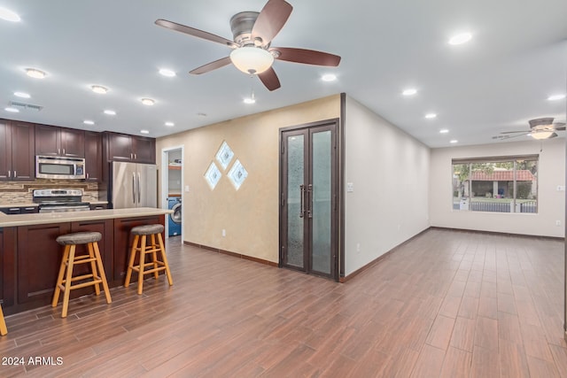 kitchen featuring a breakfast bar, tasteful backsplash, dark hardwood / wood-style flooring, washer / dryer, and stainless steel appliances