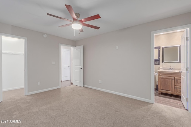 unfurnished bedroom with light carpet, ceiling fan, a spacious closet, connected bathroom, and a closet