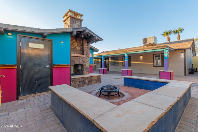 view of patio / terrace with central AC unit, an outdoor stone fireplace, and an outdoor fire pit