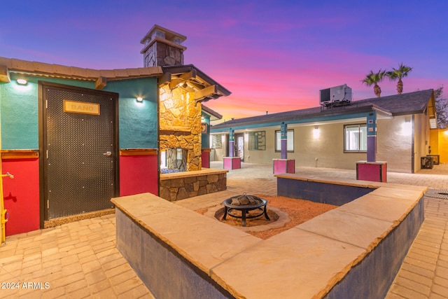 patio terrace at dusk with central air condition unit, a stone fireplace, and an outdoor fire pit