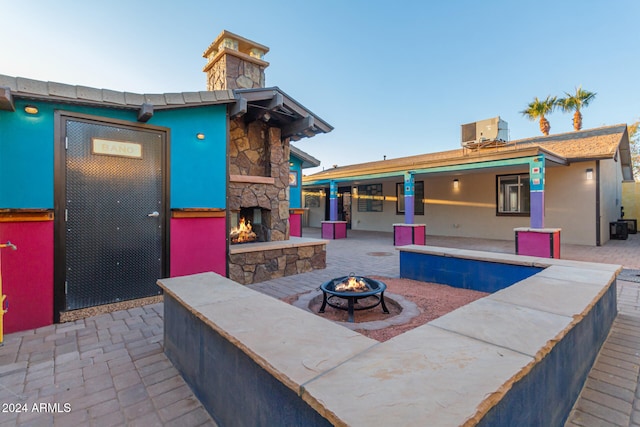 view of patio featuring a fire pit, cooling unit, and an outdoor stone fireplace