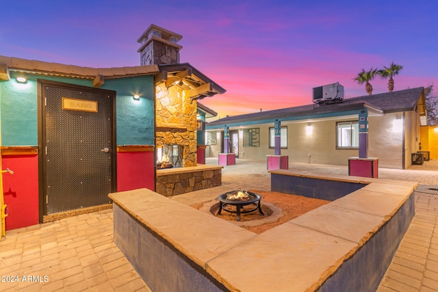 patio terrace at dusk featuring a fireplace, a fire pit, and cooling unit