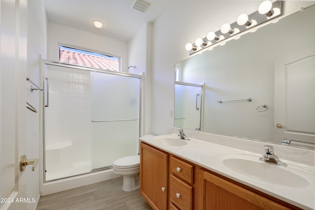 bathroom with a shower with door, vanity, wood-type flooring, and toilet