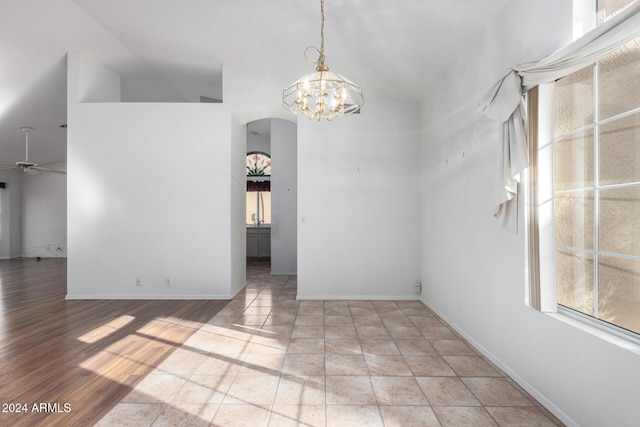 empty room featuring ceiling fan with notable chandelier, light hardwood / wood-style floors, and vaulted ceiling