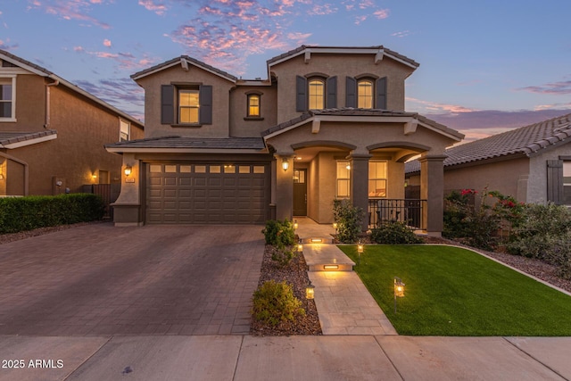 view of front of property featuring decorative driveway, a tile roof, a yard, stucco siding, and a garage