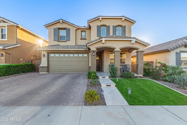 view of front of property featuring decorative driveway, stucco siding, a garage, a tiled roof, and a front lawn