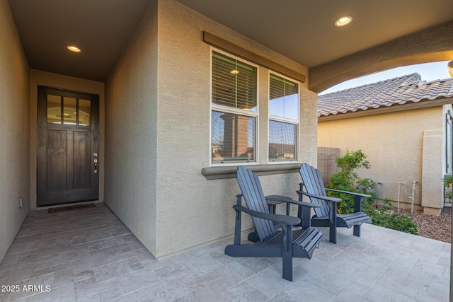 view of exterior entry with covered porch, a tile roof, and stucco siding