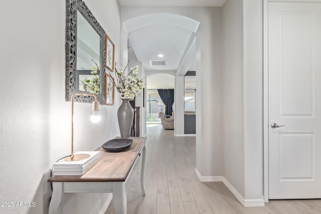 hall with arched walkways, light wood finished floors, visible vents, and baseboards