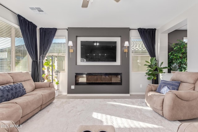 living area featuring a wealth of natural light, a glass covered fireplace, visible vents, and ceiling fan