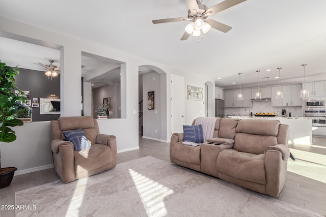 living area with arched walkways, a ceiling fan, and light wood-style floors