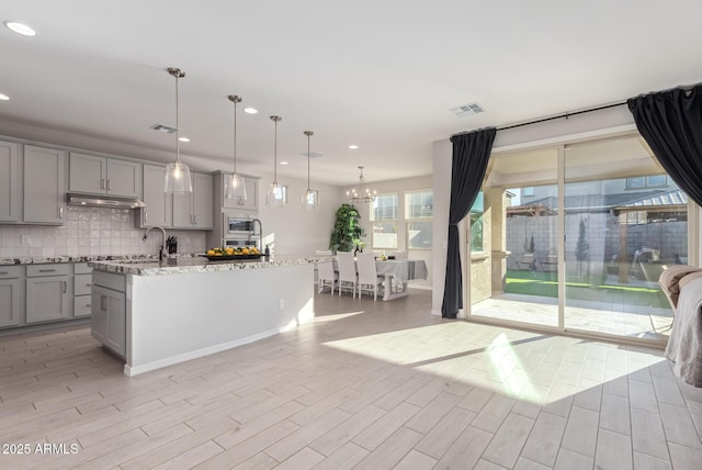 kitchen with visible vents, stainless steel microwave, gray cabinets, under cabinet range hood, and backsplash