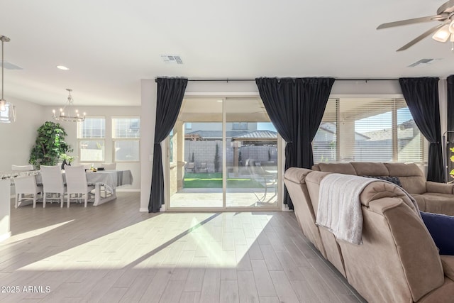 living room with ceiling fan with notable chandelier, visible vents, and wood finished floors