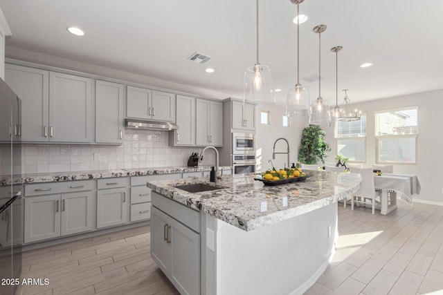 kitchen featuring visible vents, appliances with stainless steel finishes, a sink, gray cabinets, and backsplash