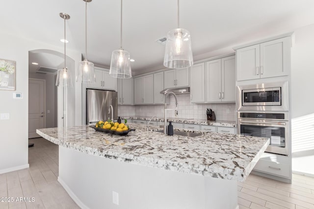 kitchen with arched walkways, visible vents, light stone countertops, stainless steel appliances, and backsplash