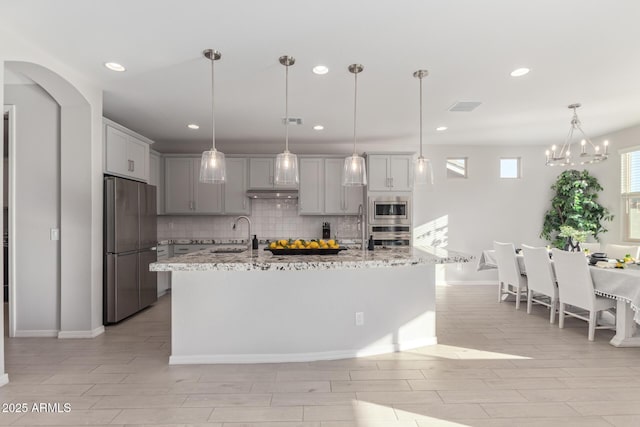 kitchen with under cabinet range hood, visible vents, appliances with stainless steel finishes, backsplash, and gray cabinets