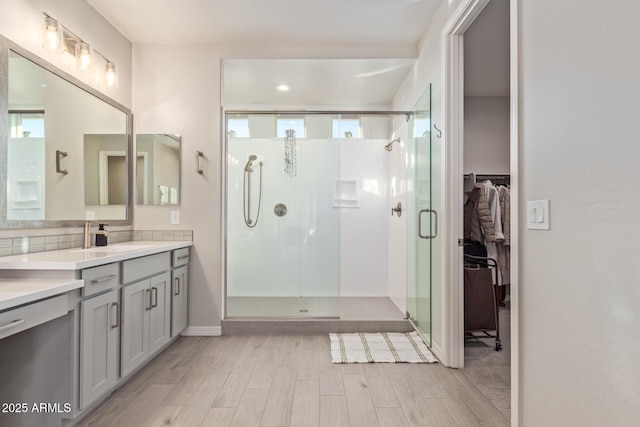 bathroom featuring backsplash, a spacious closet, a stall shower, vanity, and wood finished floors