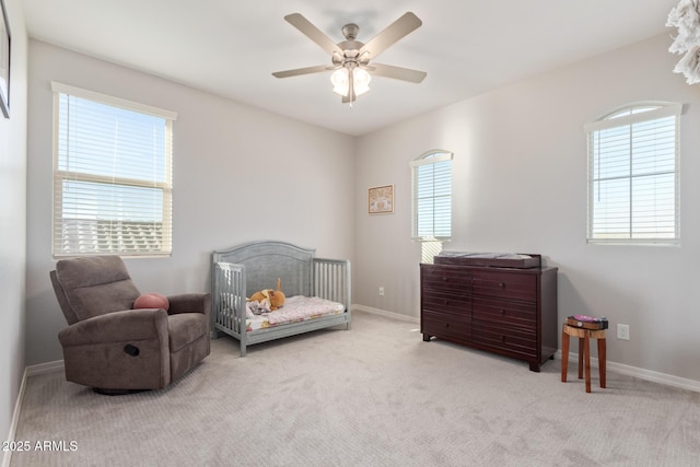 bedroom with a crib, carpet flooring, a ceiling fan, and baseboards