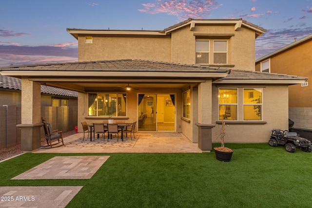 rear view of house with a yard, fence, stucco siding, and a patio