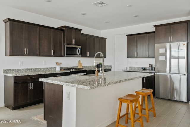 kitchen featuring dark brown cabinetry, stainless steel appliances, sink, and an island with sink