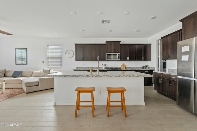 kitchen featuring appliances with stainless steel finishes, sink, a breakfast bar area, a kitchen island with sink, and light stone counters