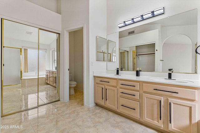 bathroom with visible vents, a washtub, toilet, double vanity, and a sink