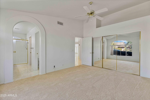 unfurnished bedroom featuring carpet, visible vents, high vaulted ceiling, ensuite bath, and arched walkways