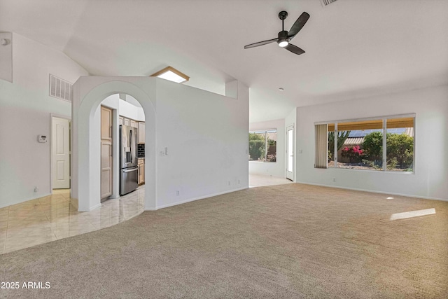 unfurnished living room featuring a ceiling fan, visible vents, light colored carpet, and arched walkways