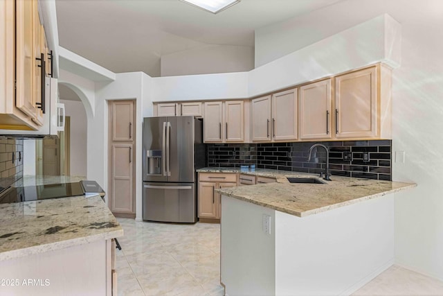 kitchen with a sink, light stone counters, stainless steel fridge, a peninsula, and decorative backsplash